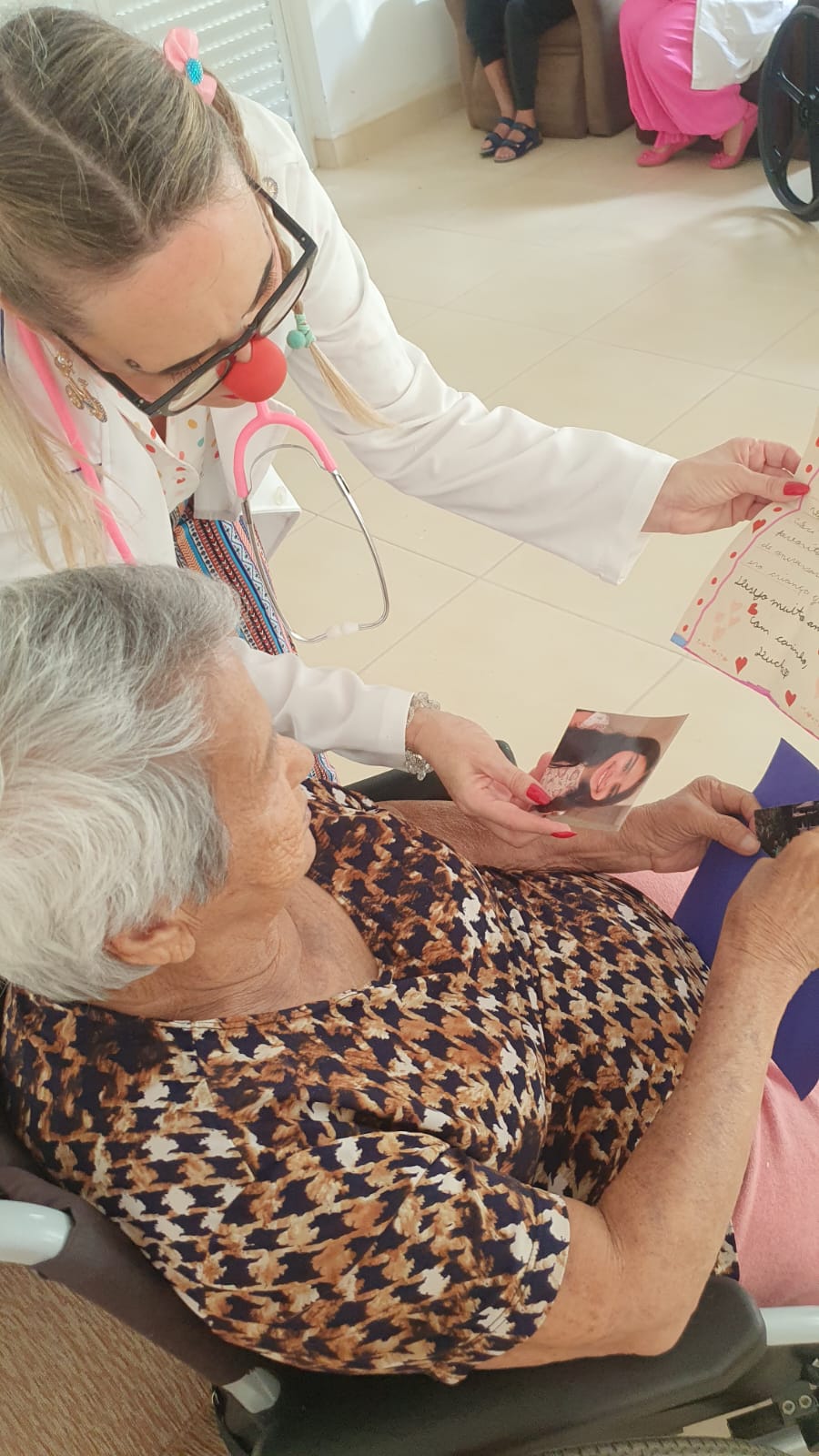 Doutora palhaça lendo carta para idosa em casa geriátrica
